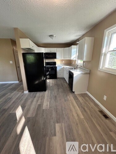 A kitchen with a black fridge and wooden flooring.
