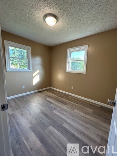 A room with wooden flooring and two windows.