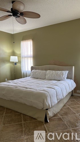 A bedroom with a bed, a ceiling fan, and a wall-mounted lamp.