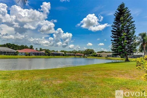A tree stands in front of a house by a lake.