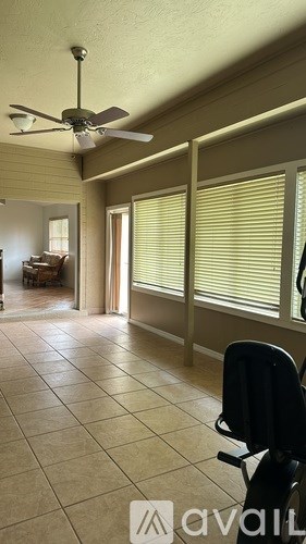 A room with a fan, tiled floor, and a chair.