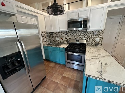 A kitchen with a stainless steel refrigerator and a black fan hanging from the ceiling.