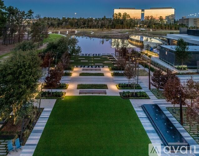A well-lit park with a pond and a building in the background.