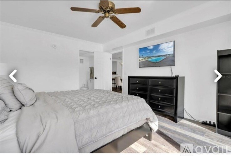 A bedroom with a large bed, a ceiling fan, and a TV mounted on the wall.
