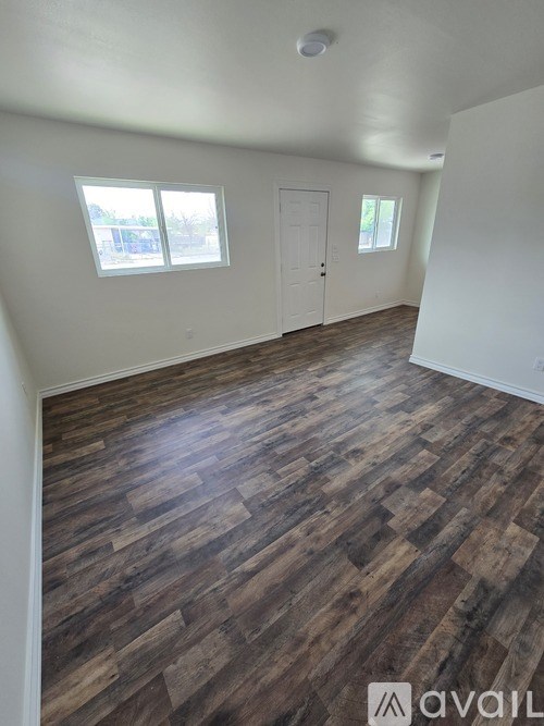 A room with wooden flooring and two windows.