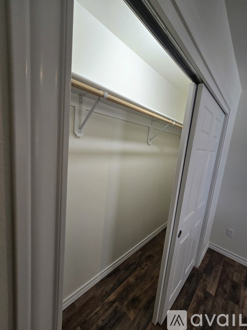 A white door is open to a room with a white wall and a wooden floor.