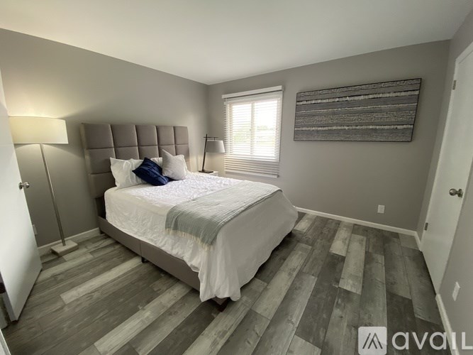 A bedroom with a bed, lamp, and wooden flooring.