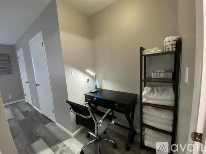 A room with a black desk and chair, a shelf with folded towels, and a cabinet with a mirror.