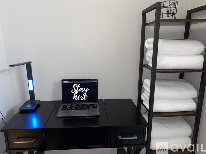 A laptop with a "Stay here" sign on the lid is placed on a black desk.
