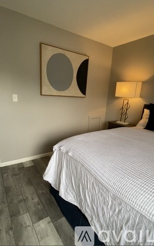 A bedroom with a bed, lamp, and a picture on the wall.