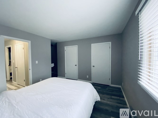 A bedroom with a bed, two closets, and a window with blinds.