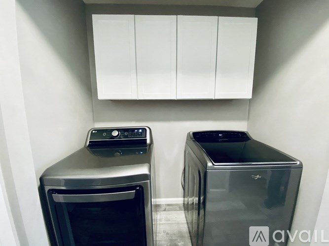 Two black trash bins in a corner of a room with white cupboards.