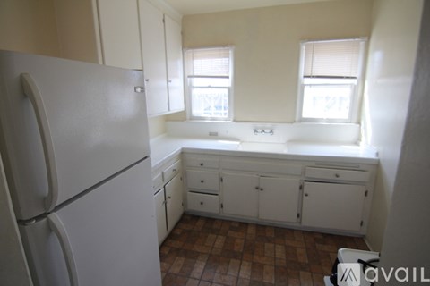A kitchen with a fridge, cupboards and a window.