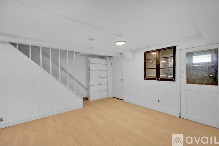 A spacious room with wooden floors and a staircase with a glass railing.