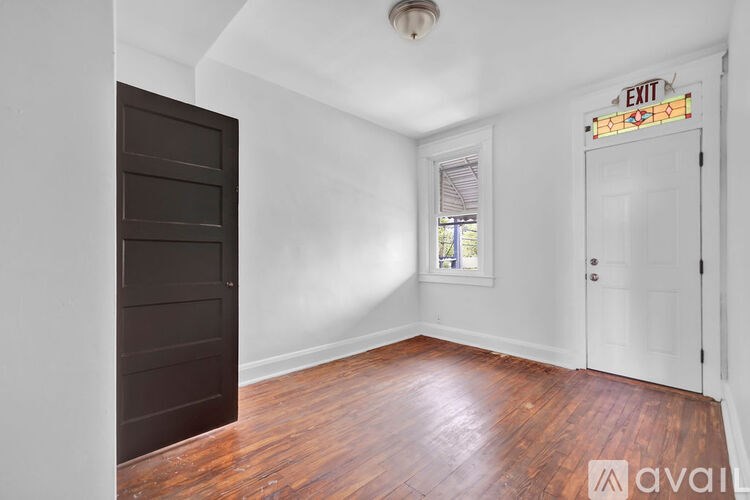 A room with a wooden floor and white walls, with a door on the right and a window on the left.