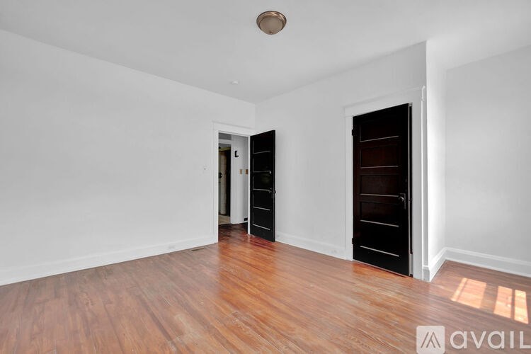A room with wooden floors and white walls, with a door on the right and another door on the left.