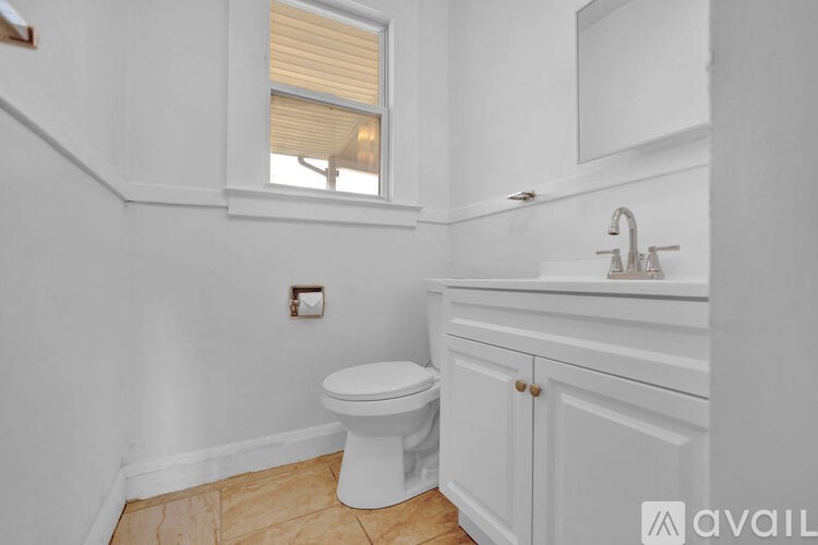 A white toilet sits in a bathroom with a sink and a window.