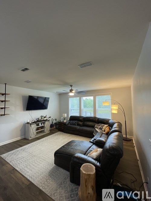 A living room with a black leather couch and a flat screen TV mounted on the wall.