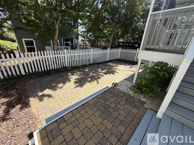 A backyard with a white picket fence and a brick patio.