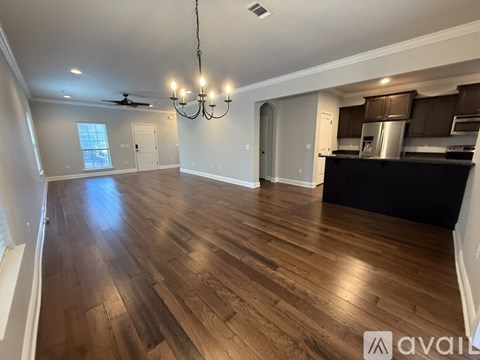 A spacious room with wooden flooring and a kitchen area in the background.