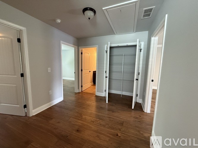 A room with white walls and wooden flooring, with a door on the left and a closet with a glass door on the right.
