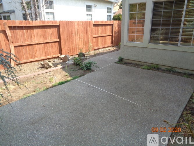 A concrete patio with a wooden fence and a house in the background.