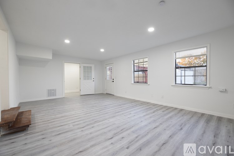 A spacious room with wooden flooring and two windows.
