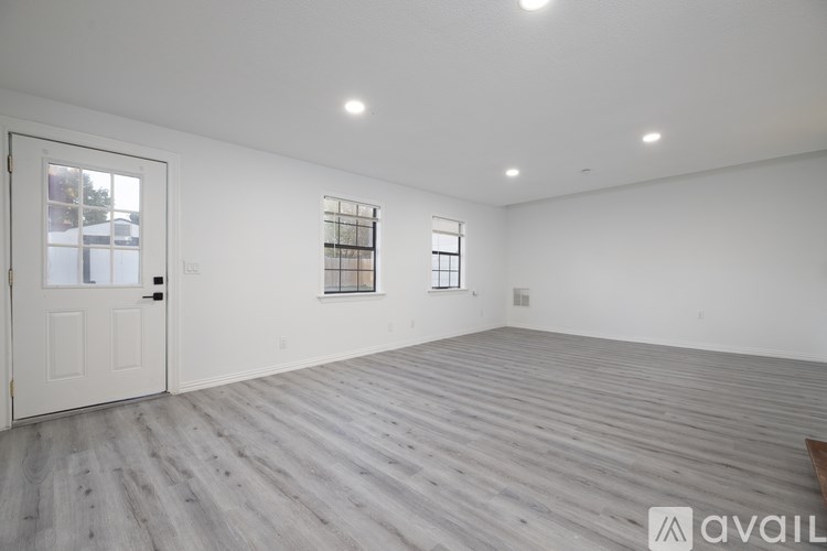 A spacious room with wooden flooring and two windows.