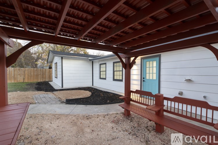 A wooden pergola with a red roof is over a small white house with a blue door.