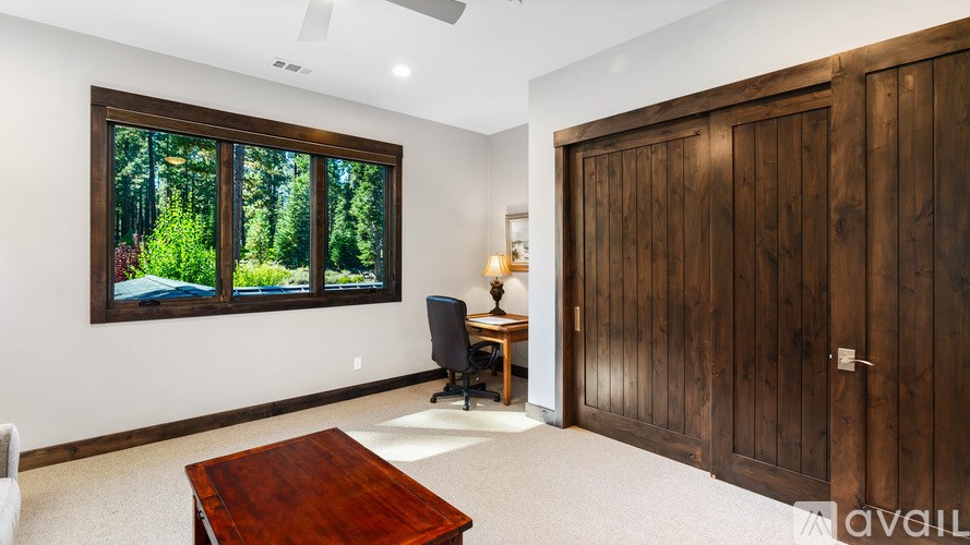 A room with a wooden table and a chair in front of a window with a view of trees.