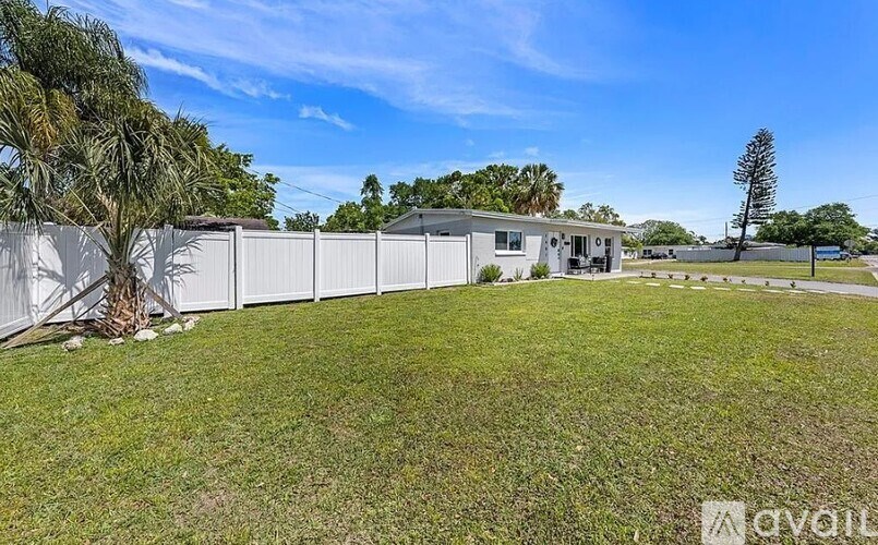 A white fence surrounds a grassy area with a house in the background.