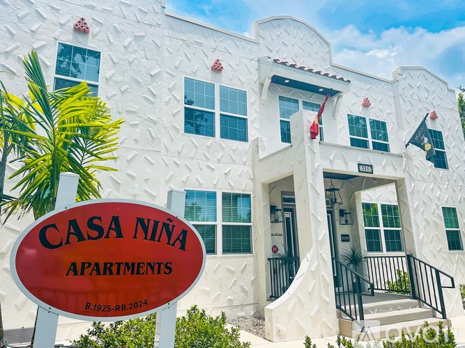 A white building with a red sign that says "Casa Nina Apartments" in front of it.