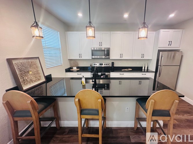 A kitchen with white cabinets and a black countertop with a framed picture on the left.