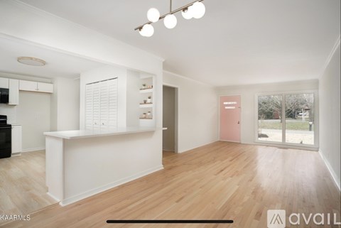 A spacious room with wooden flooring and a kitchen area with white cabinets and appliances.