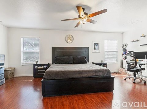 A bedroom with a large bed, a ceiling fan, and a desk with a chair.