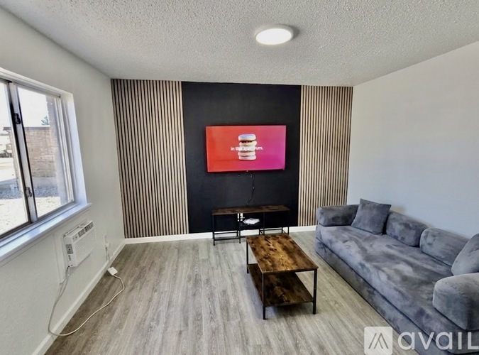 A living room with a grey couch, a wooden coffee table, and a flat screen TV mounted on the wall.