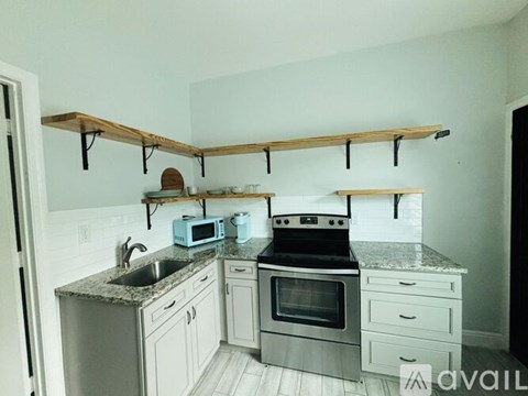 A kitchen with white cabinets and a wooden shelf above the counter.