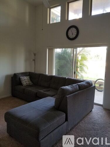 A living room with a grey couch and a clock on the wall.