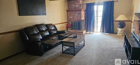 A living room with a black leather couch and a fireplace.