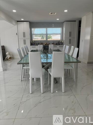 A modern dining room with a glass table and white chairs.