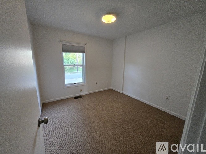 A room with a carpeted floor, a window with blinds, and a door leading to another room.