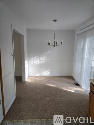 A room with a carpeted floor, a chandelier, and a window with curtains.