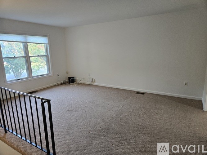 A room with a carpeted floor and a window with a view of trees and a building outside.