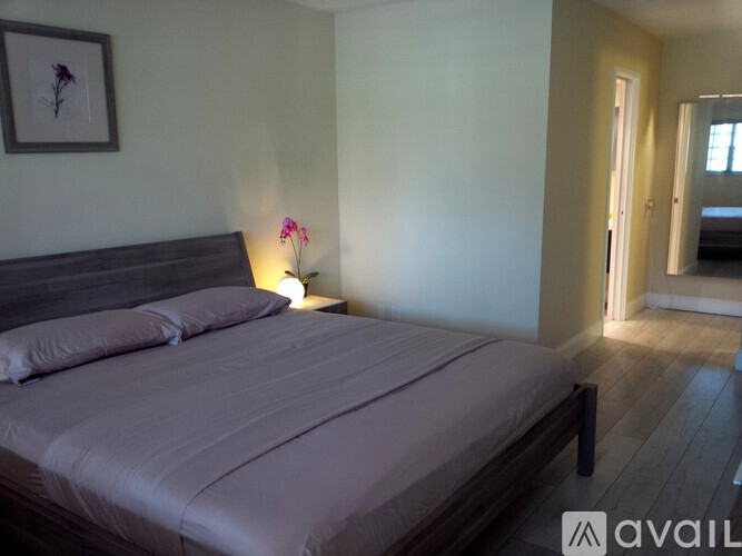 A bedroom with a bed, a nightstand with a lamp, and a picture on the wall.