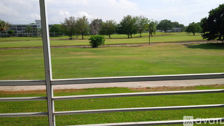 A grassy field with a fence in the foreground and trees in the distance.
