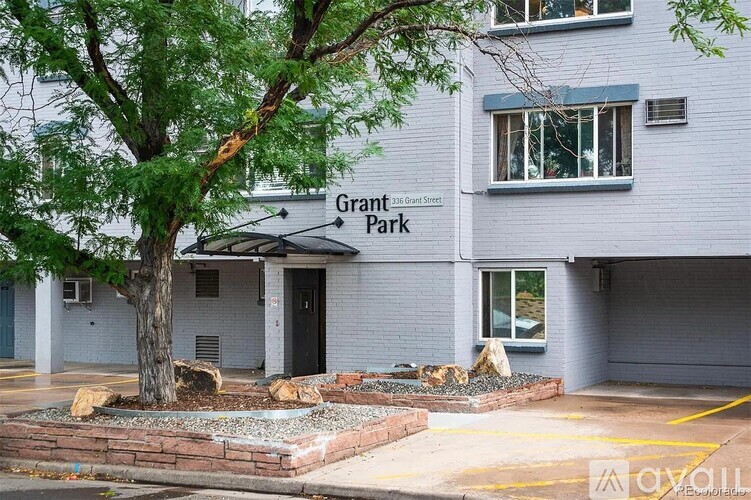 A tree in front of a grey building with the words Grant Ave Park on it.