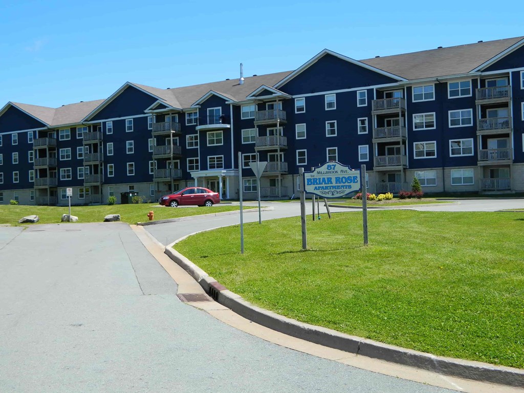A red car is parked in front of a blue apartment building.