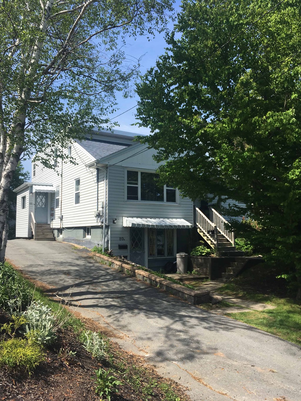 A white house with a grey roof and a tree in front of it.