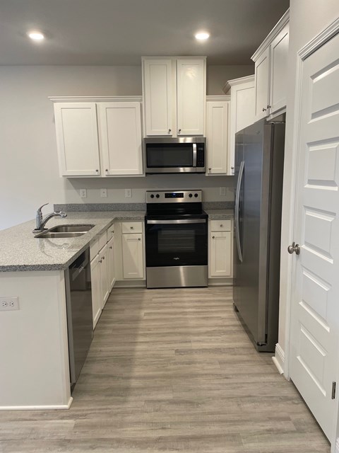 A kitchen with white cabinets and a black microwave above the stove.