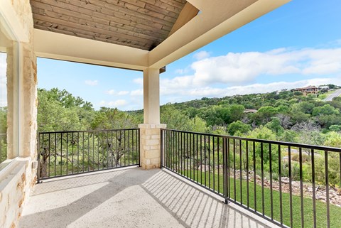 A balcony with a black railing and a view of a green landscape.